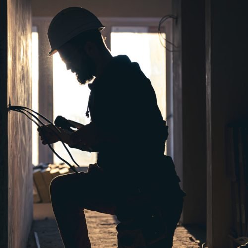 A construction electrician cuts a voltage cable during a repair, silhouette in the light of the setting sun.